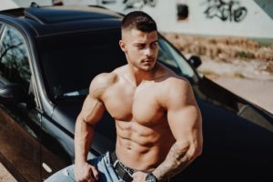 Male bodybuilder shirtless sitting on car